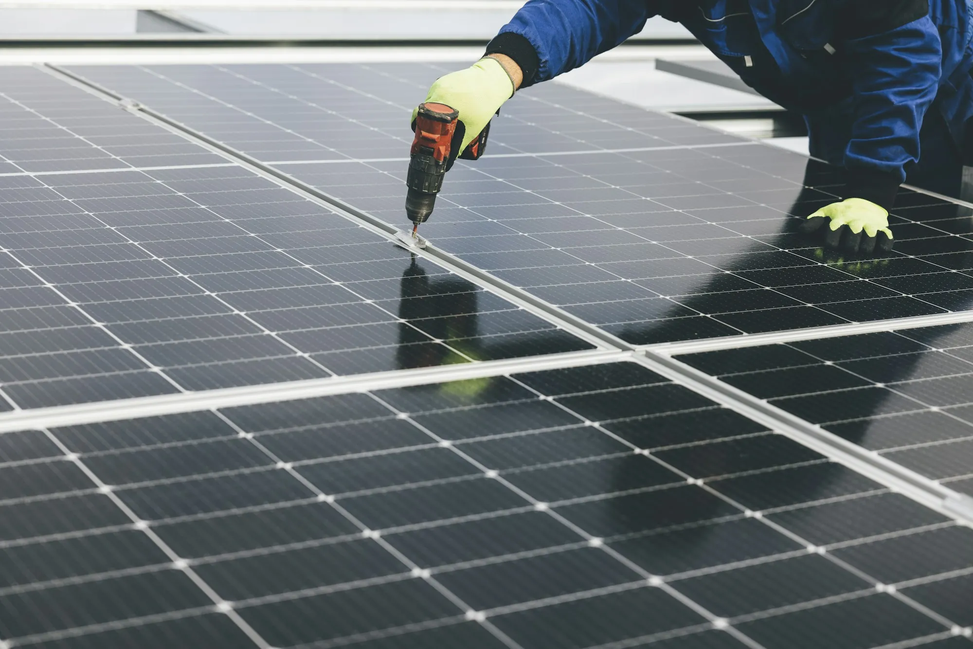 Gloved hands driving a screw into the frame of a rooftop solar panel