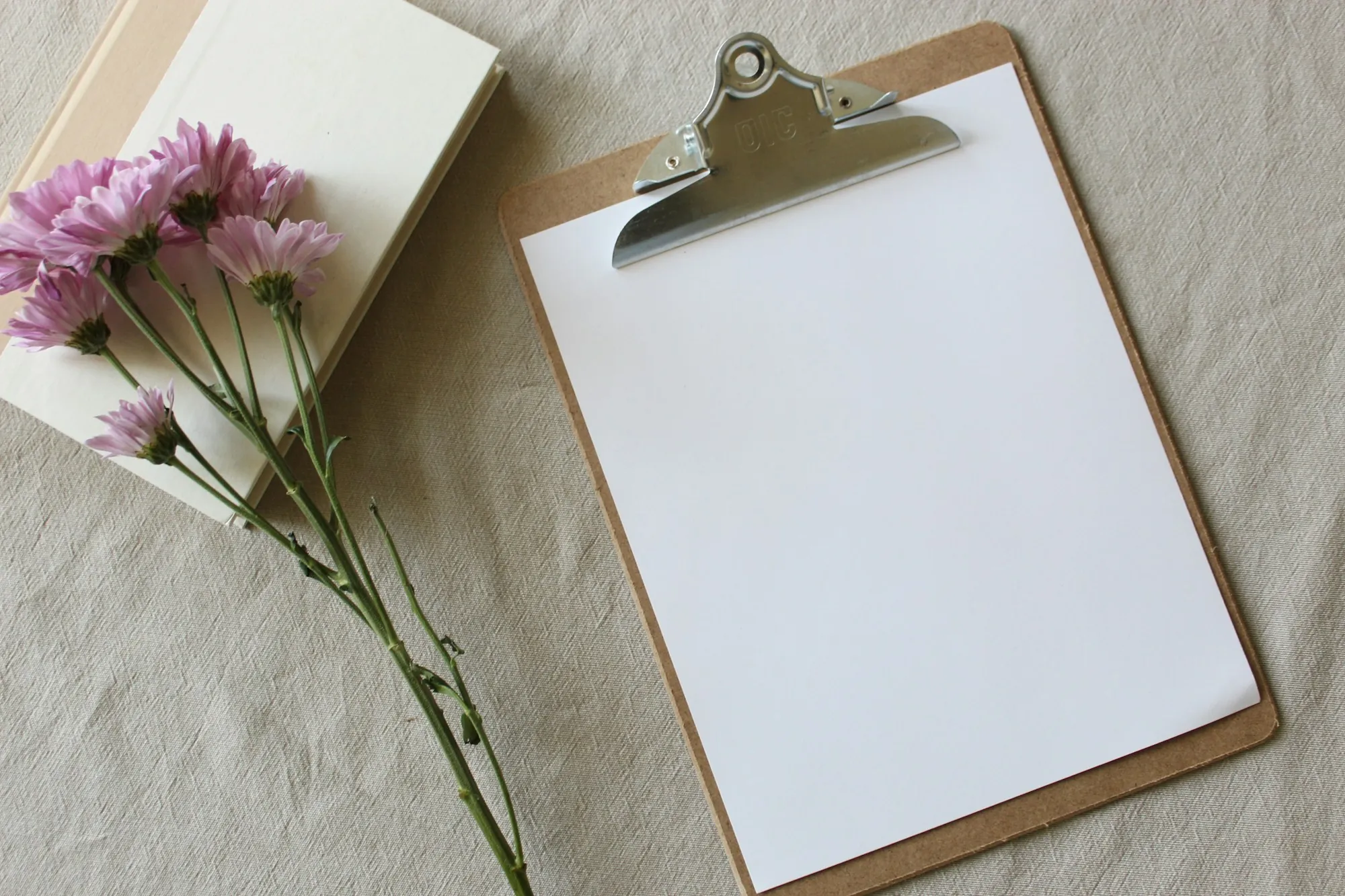 Blank clipboard on a table with a few purple flowers