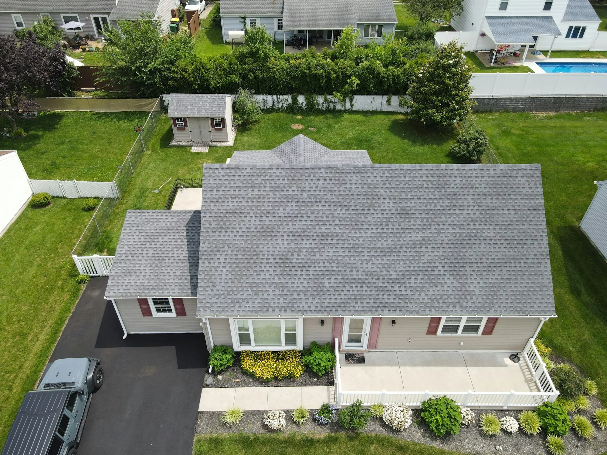 Aerial view of a single-story house with a gray shingle roof and green yard