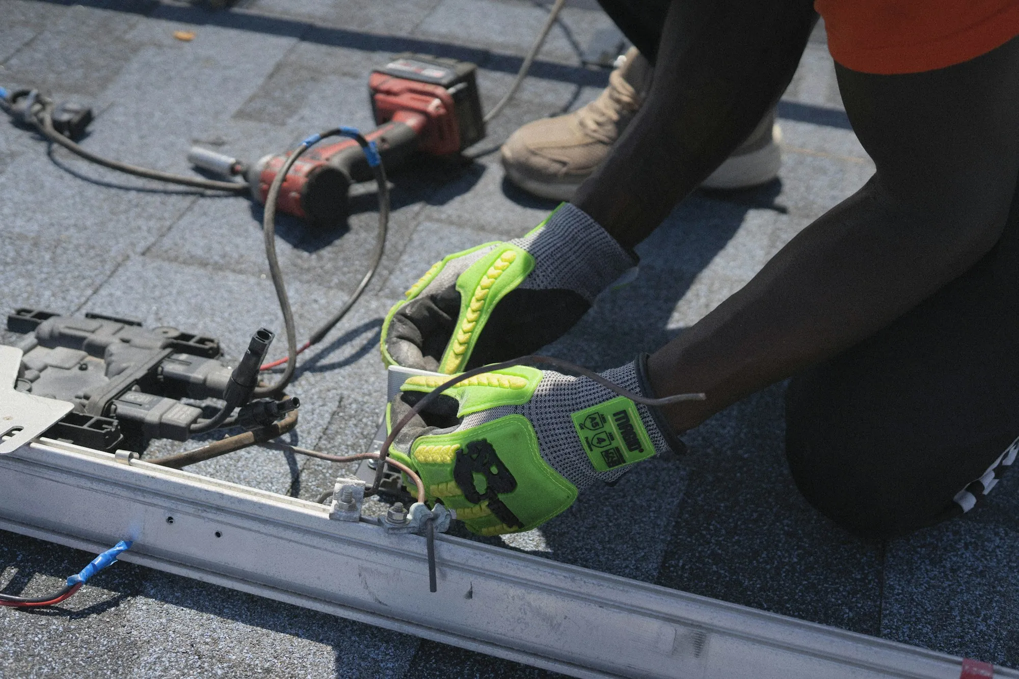 Gloved hands connecting wiring on solar racking over a shingle roof