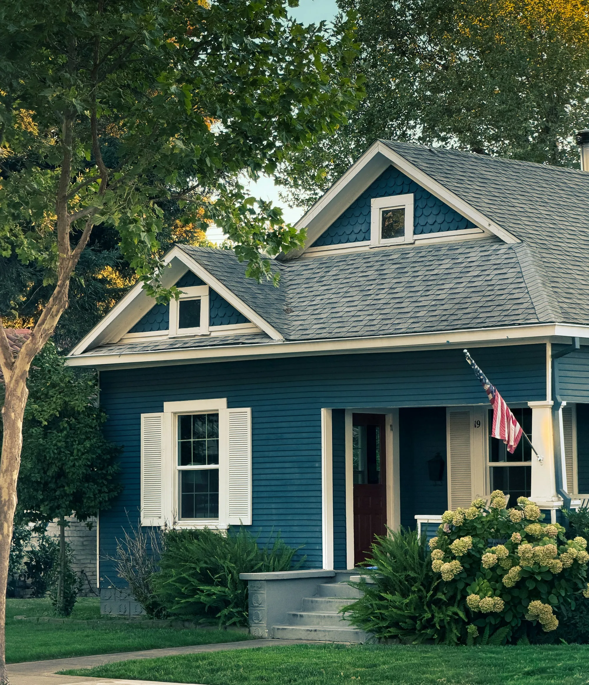Blue-sided house with white shutters and an American flag